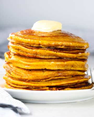 A stack of pumpkin pancakes with butter and syrup.