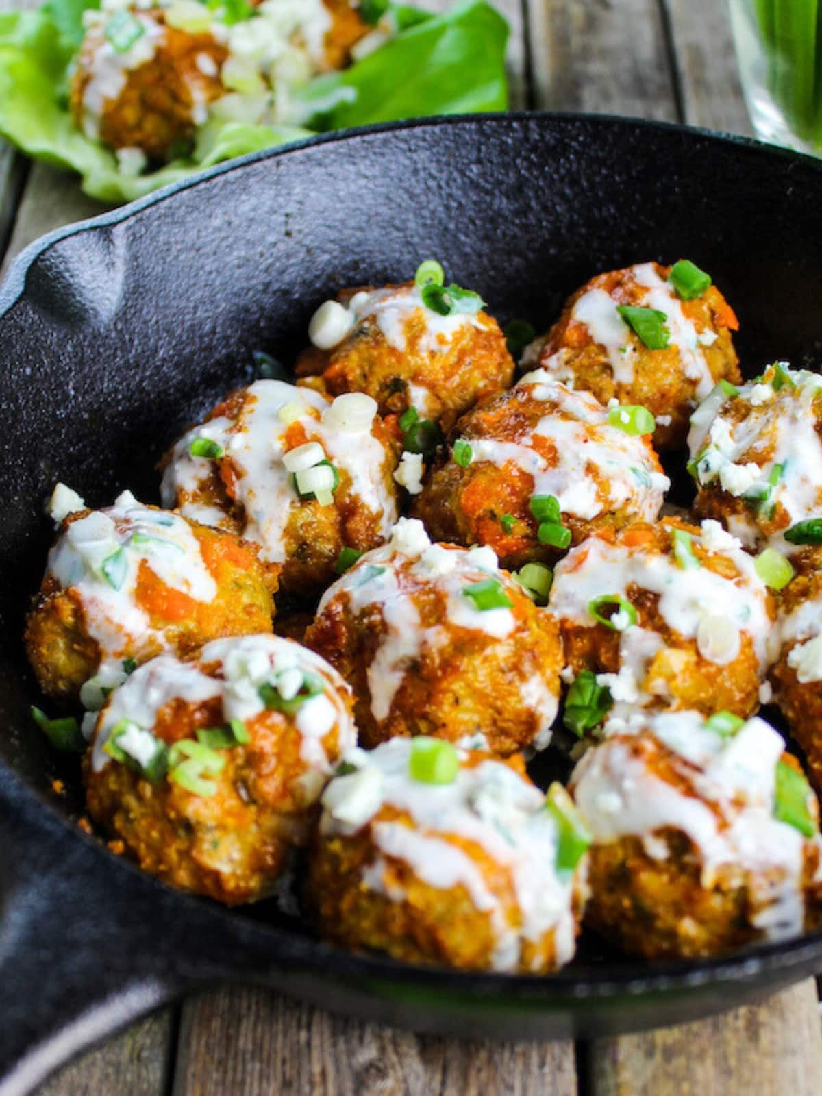 Buffalo Chicken Meatballs in a skillet with a drizzle of blue cheese sauce.