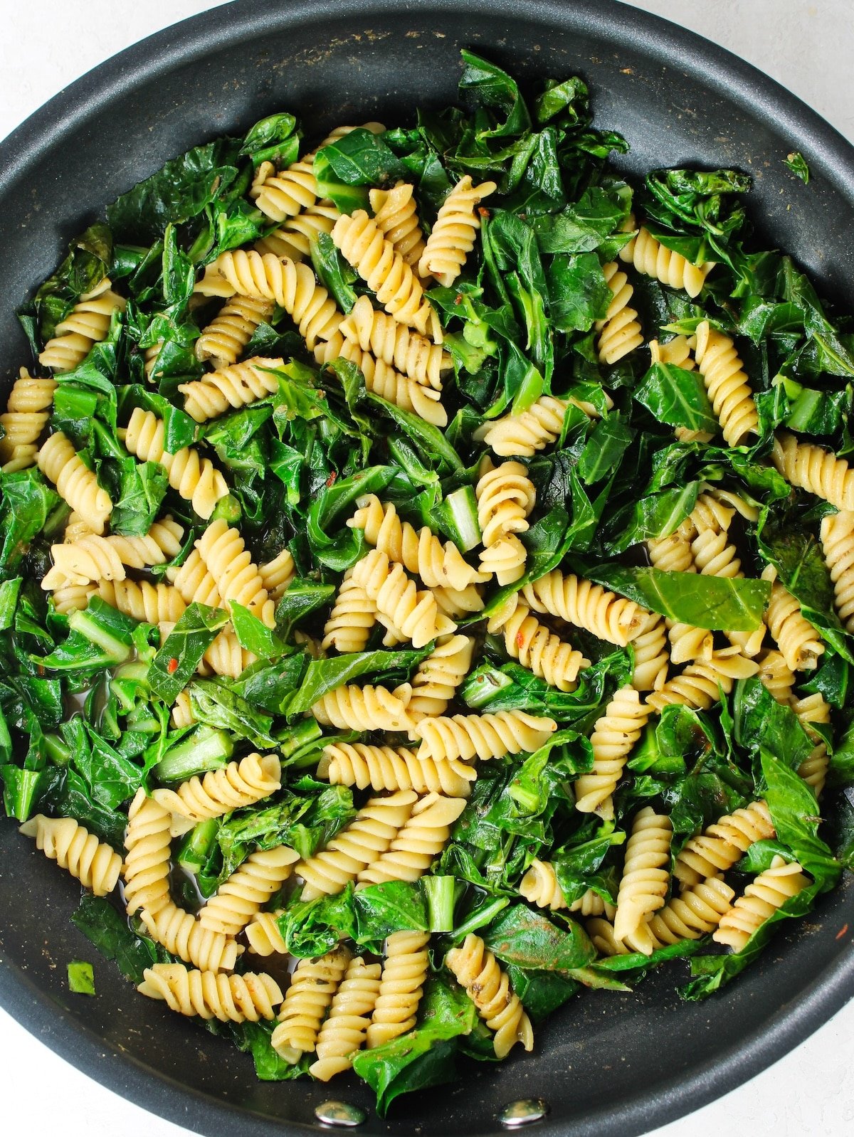 Herbs, seasoning, pasta and greens cooking in a pan.