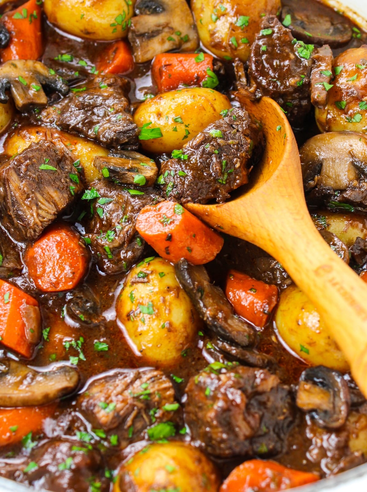A close-up photo of beef stew in a pot with a wooden spoon.