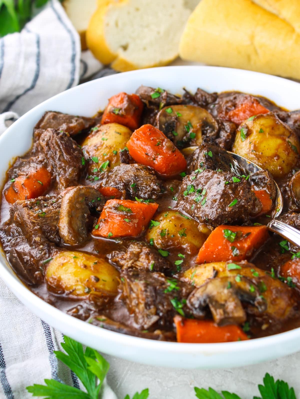 Stew in a bowl with beef, carrots, and potatoes with bread on the side.