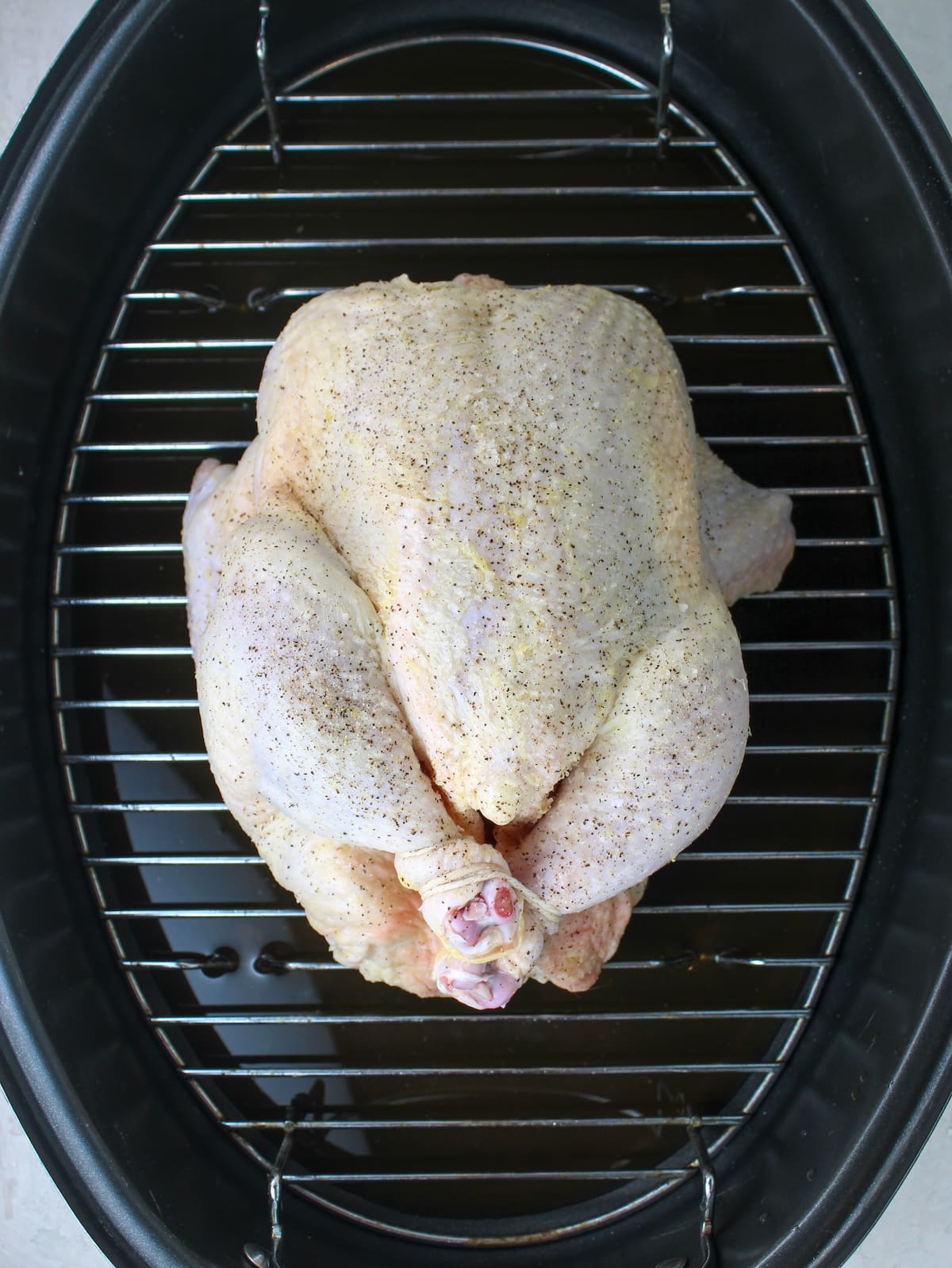 A raw whole chicken in a roasting pan, ready to be cooked in the oven.