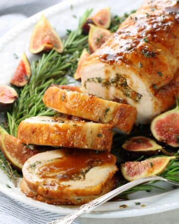 A 1200x1200 photo of a pork loin sliced on serving platter with fig sauce and figs.