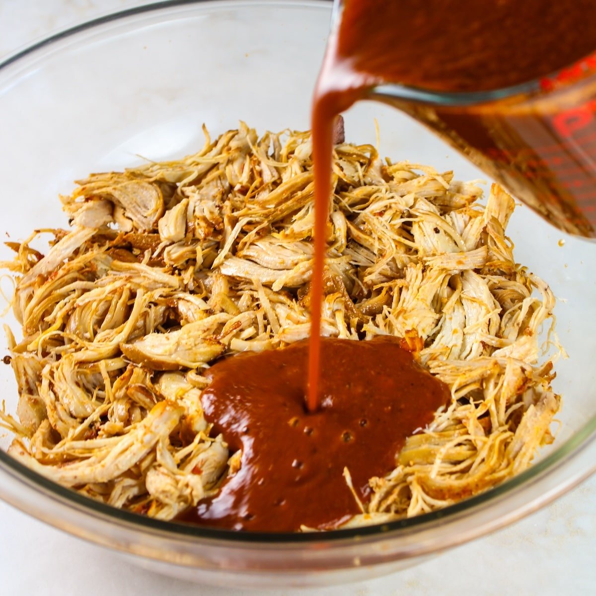 Pouring the sauce over the shredded chicken.