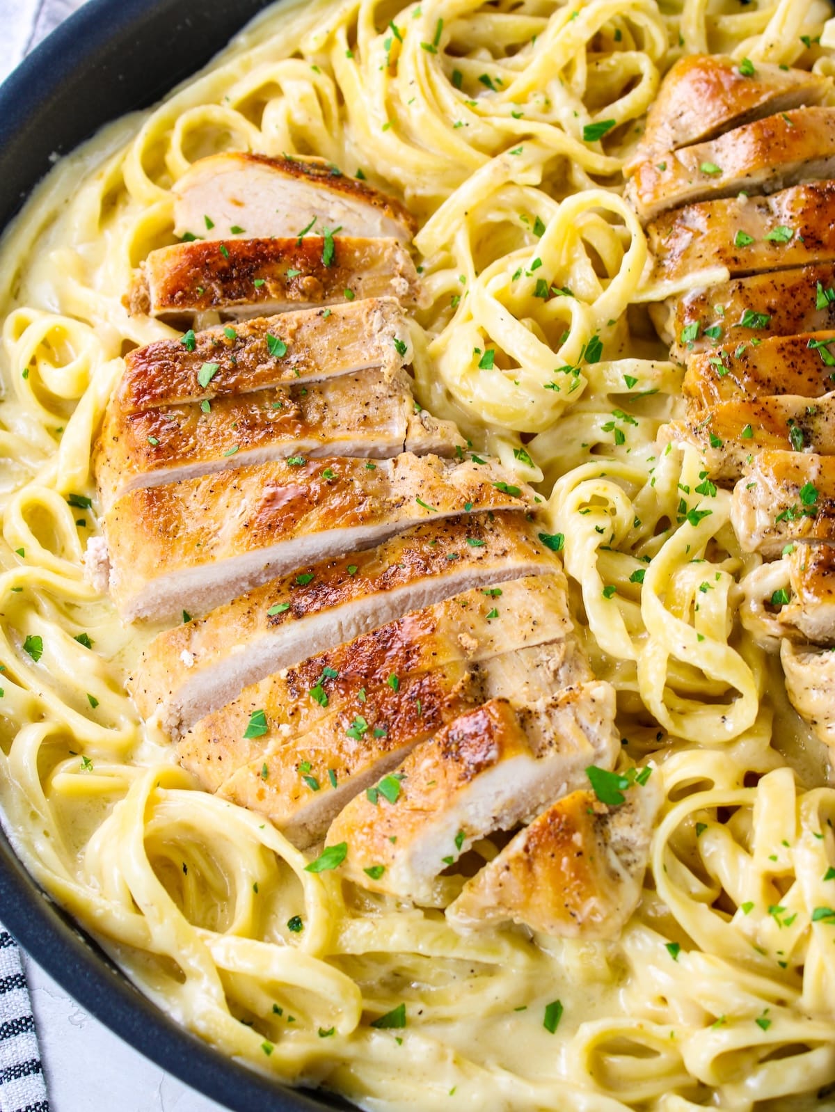 Chicken Alfredo in a pan with fettuccine noodles in a pan.
