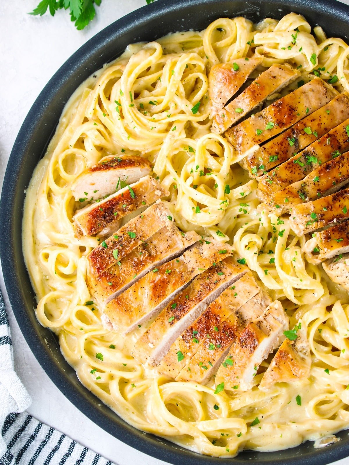 Close-up of photo of chicken with pasta and Alfredo sauce in a pan.
