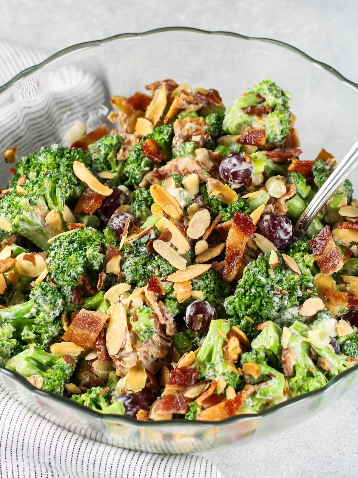 Broccoli salad with grapes and bacon in a glass bowl with a spoon.