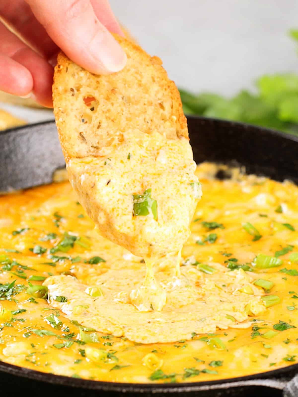 Bread being dunked into a skillet of Cheesy Buffalo Shrimp Dip.