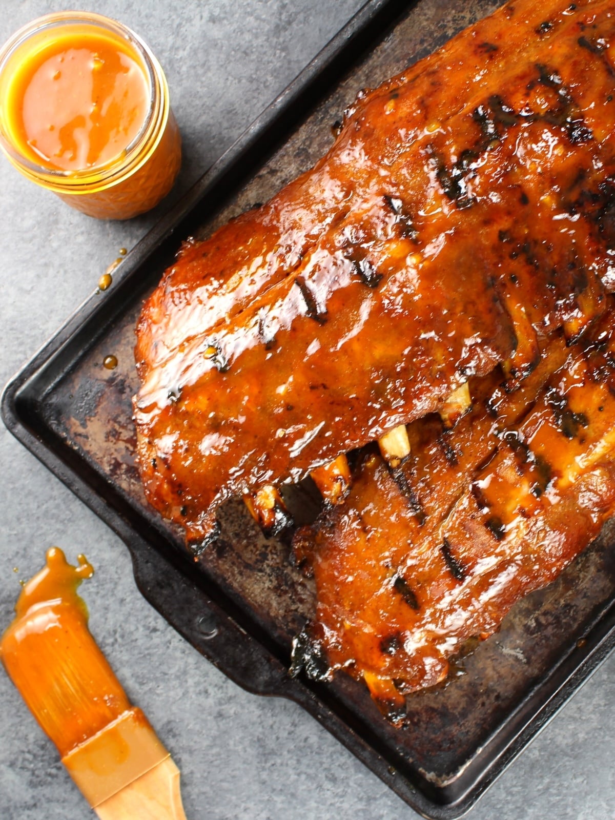 A baking sheet with grilled Secret Sauce BBQ Baby Back Ribs with extra sauce o the side.
