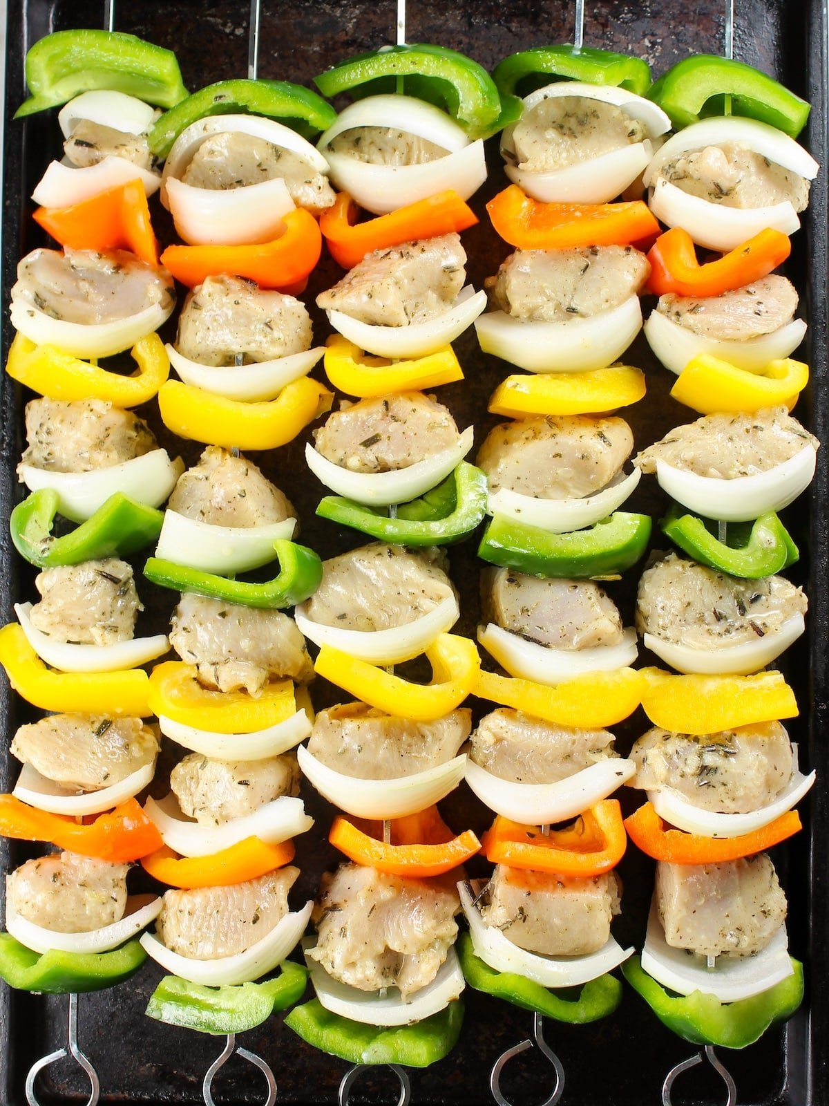 Raw chicken Kabobs skewered on baking sheet ready to cook.