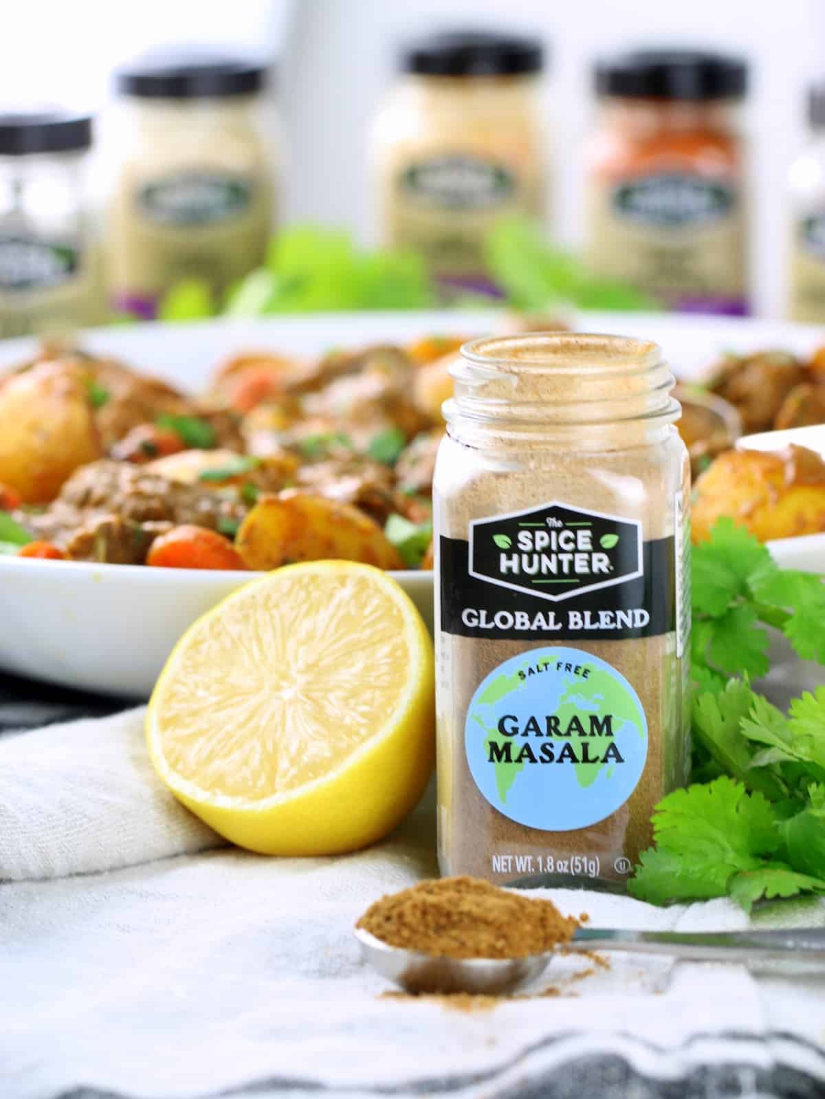 An eye level photo of a container of Garam Masala spice in the foreground.