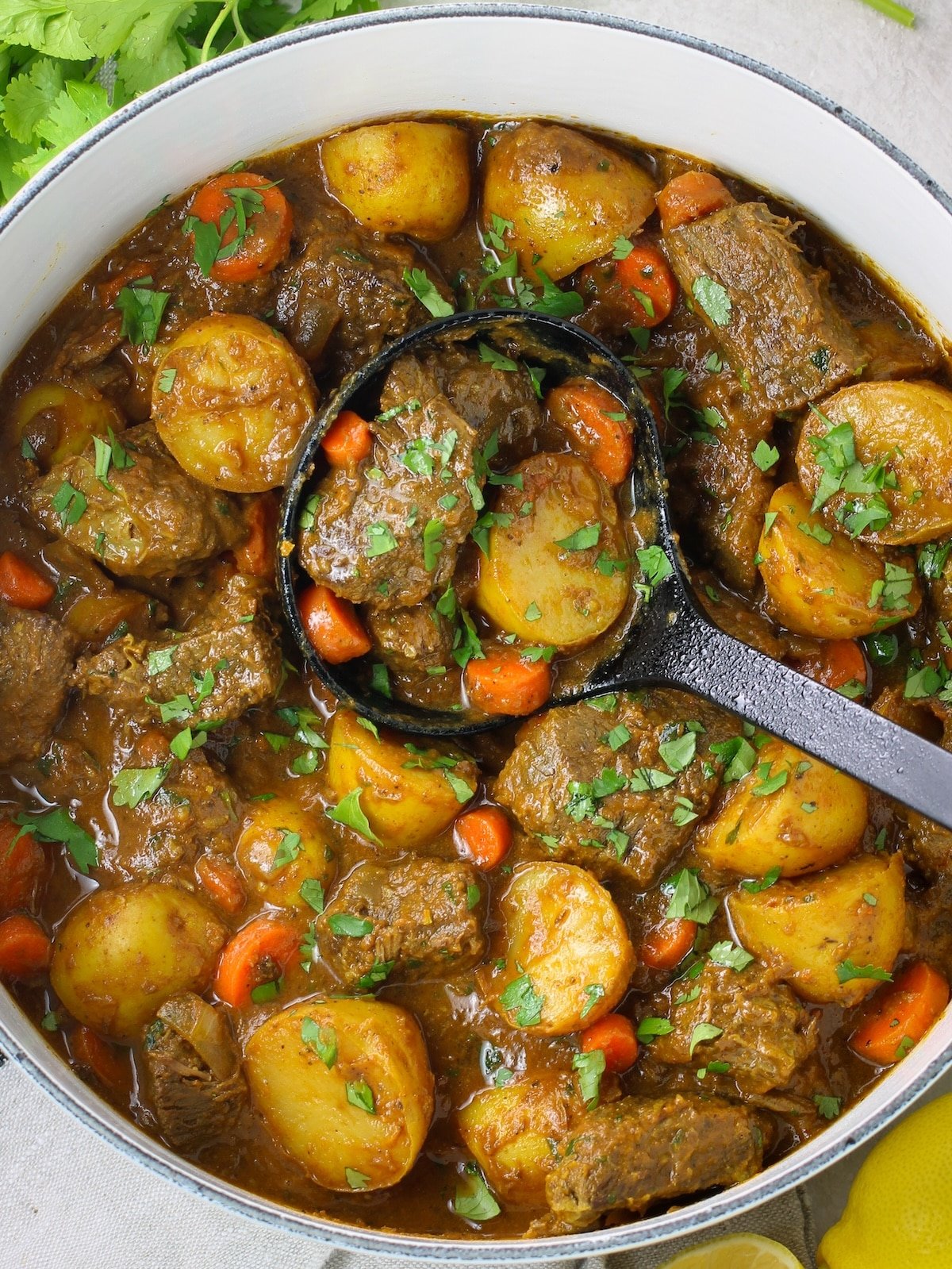 A soup pot with cooked beef, potatoes, other vegetables, beef stock and Indian spices.