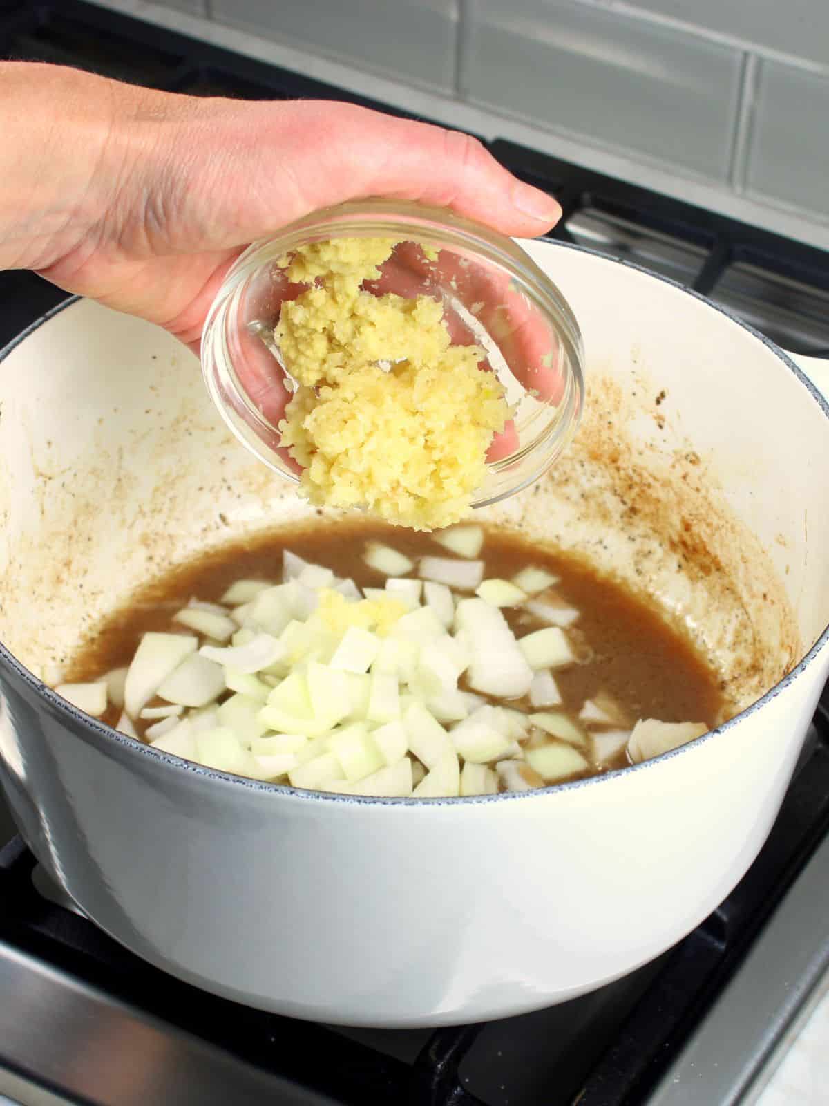 Adding garlic to a soup pot with cooked onions..