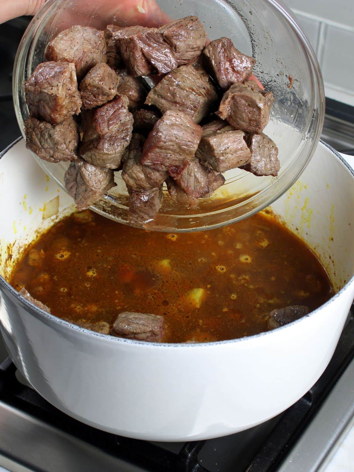 Adding seared cubes of chuck roast into a large pot with the other curry ingredients.