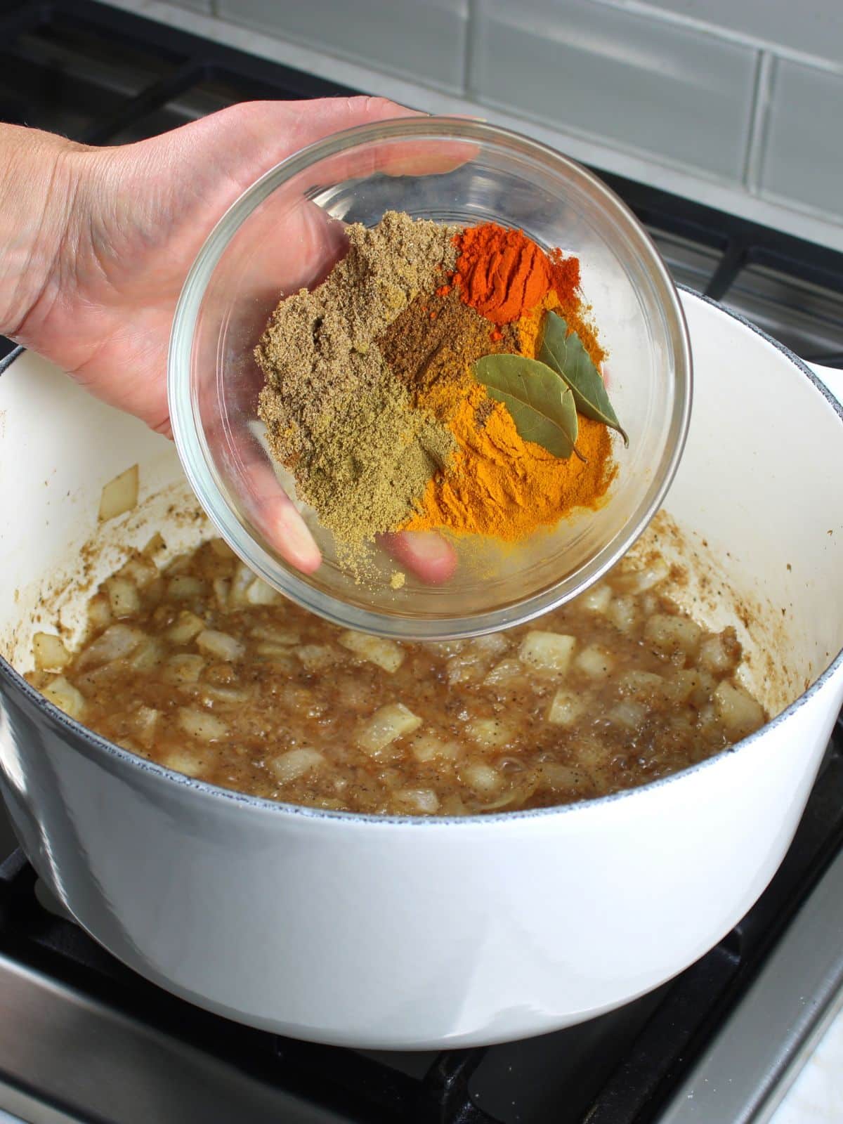 Adding Indian spices to a soup pot with cooked onions and garlic.