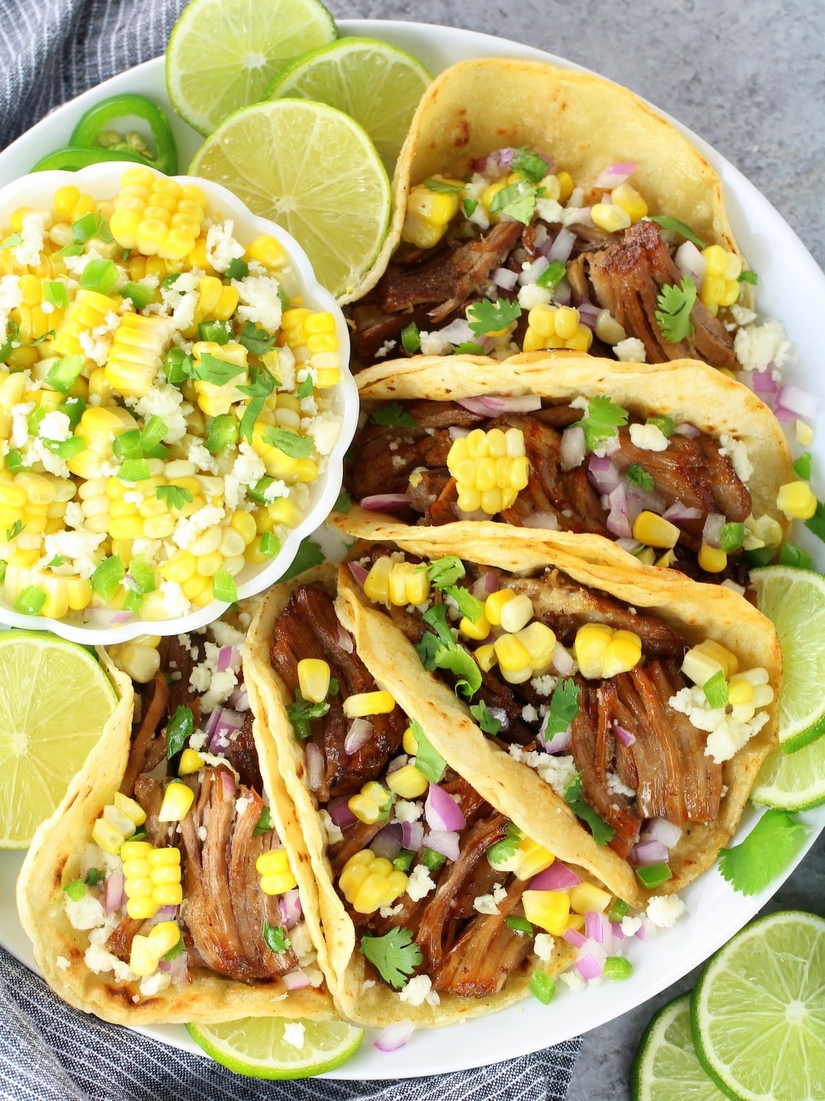 A plate of carnitas meat in taco shells with a corn salad on the side.