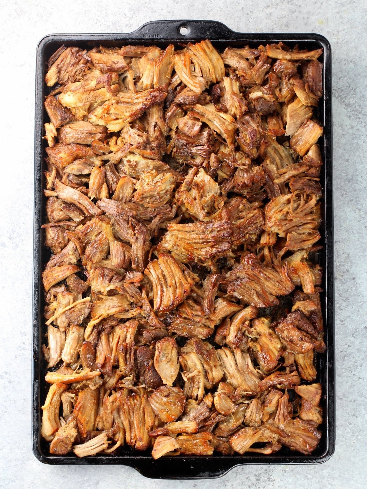 A baking sheet with the meat cooked and pulled.