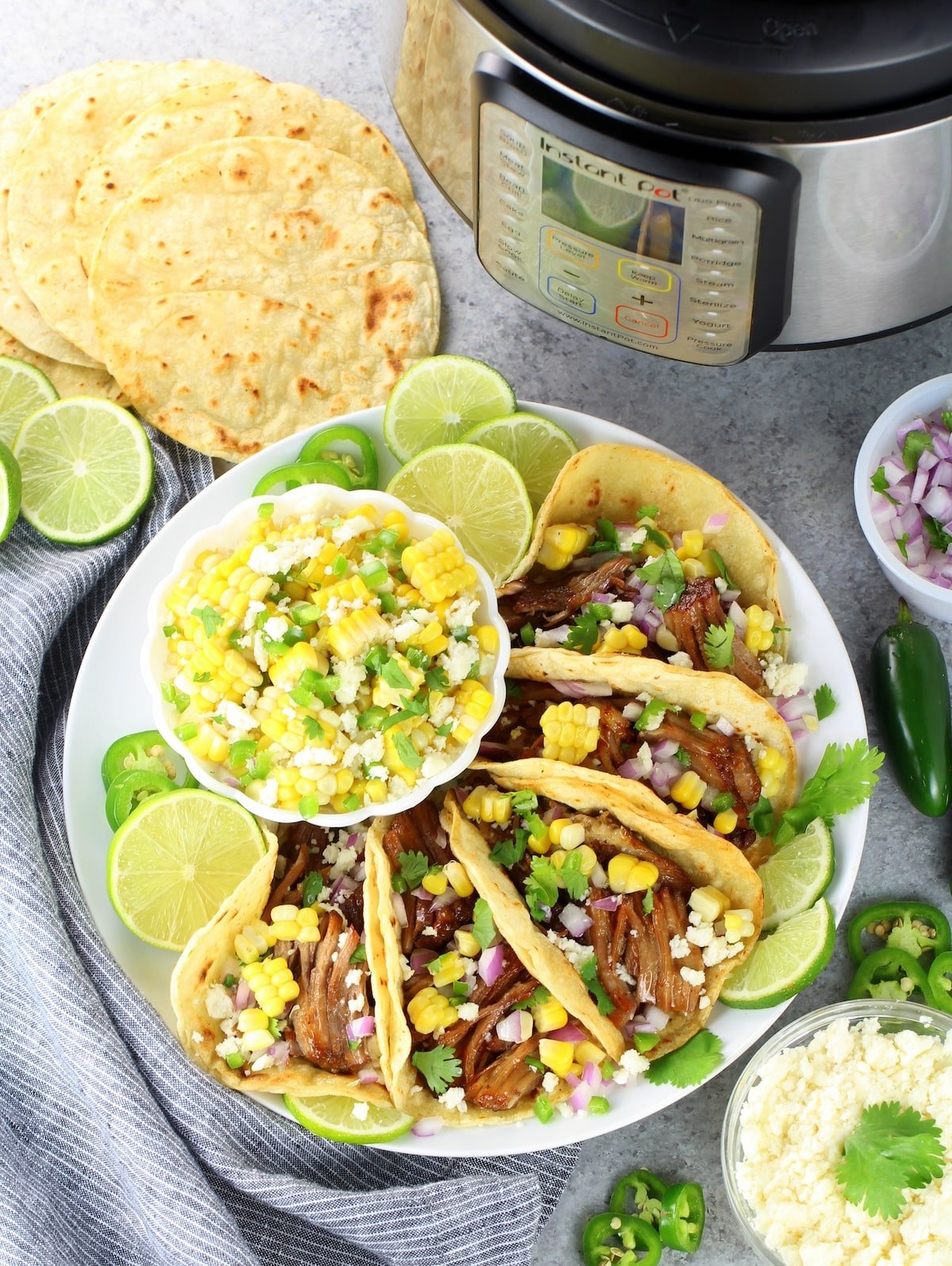 Pork carnitas meat in taco shells on a plate next to Instant Pot.