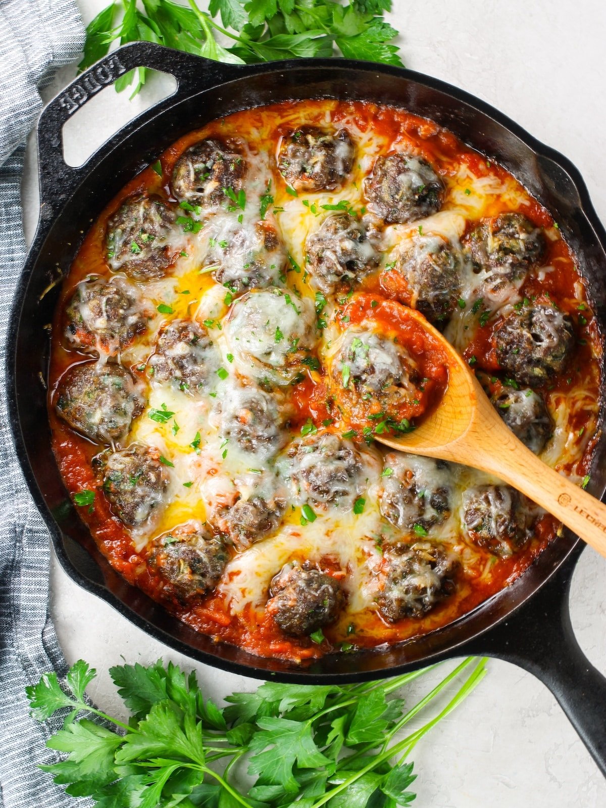 A cast iron skillet full of meatballs smothered in marinara and melted cheese.