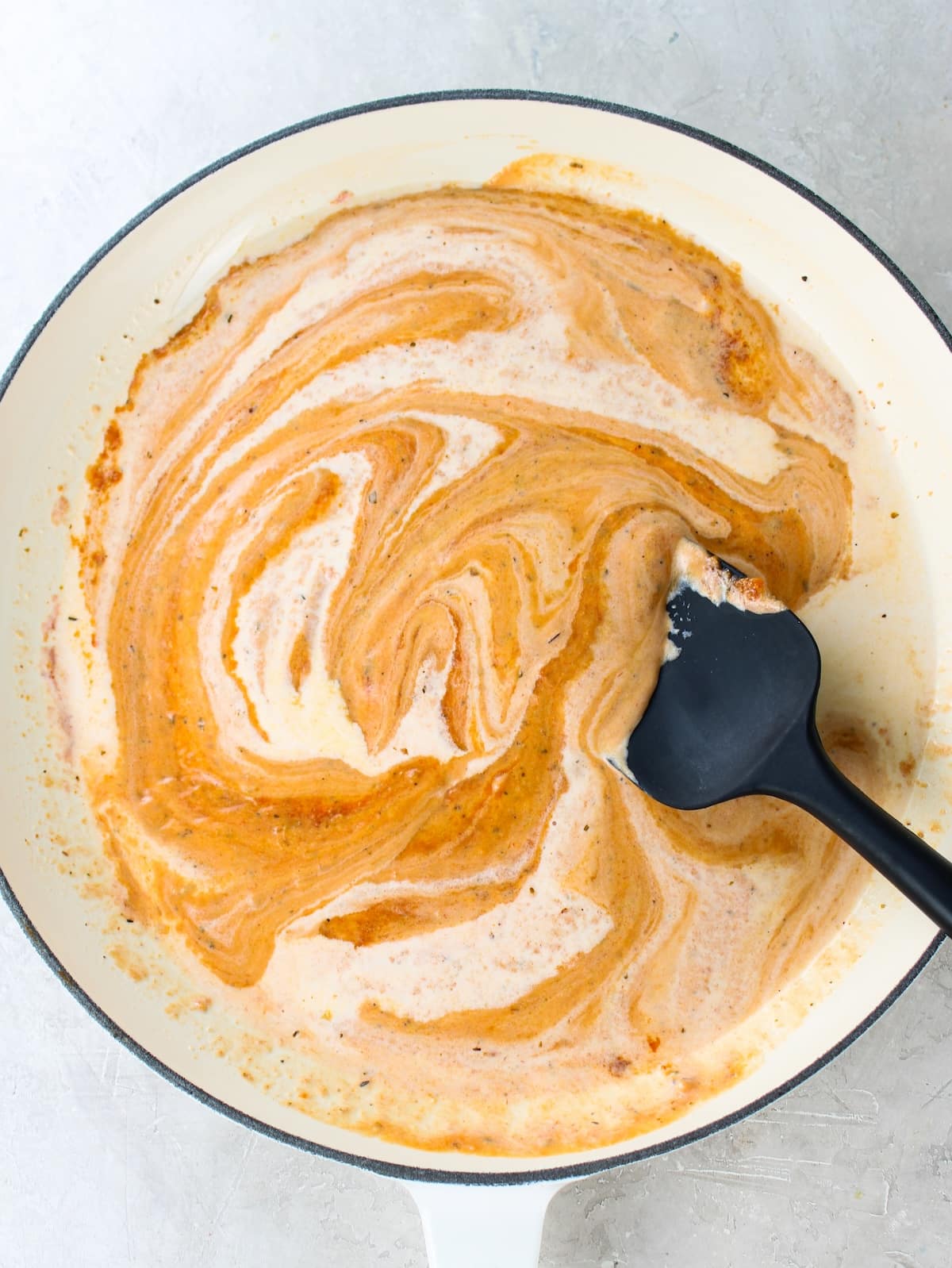 Stirring heavy cream into tomato sauce in a skillet.