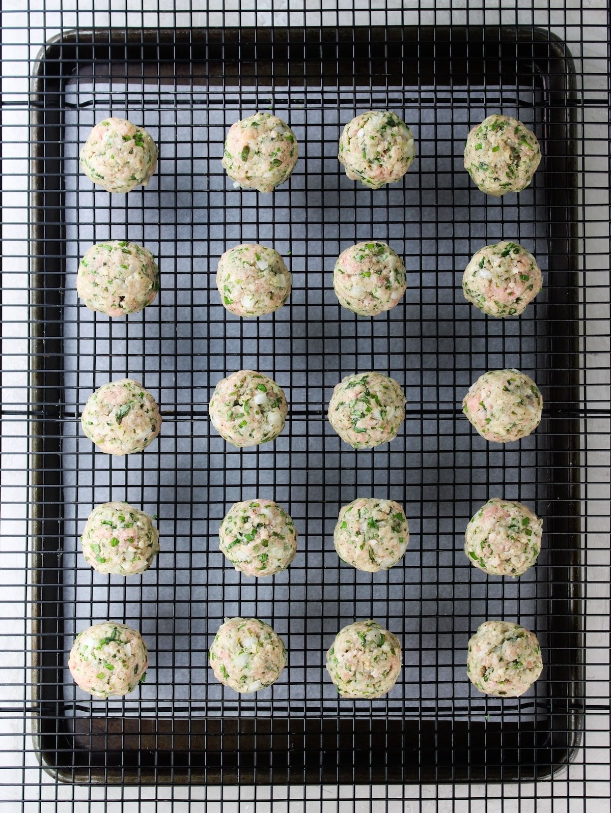 Raw meatballs on a wire rack over a sheet pan ready to be baked in the oven.