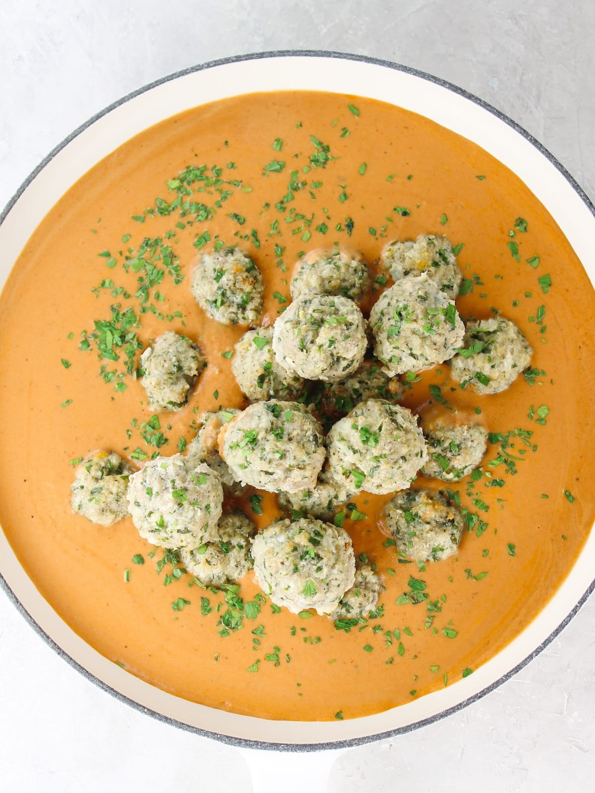 Adding meatballs to tomato cream sauce in a pan.