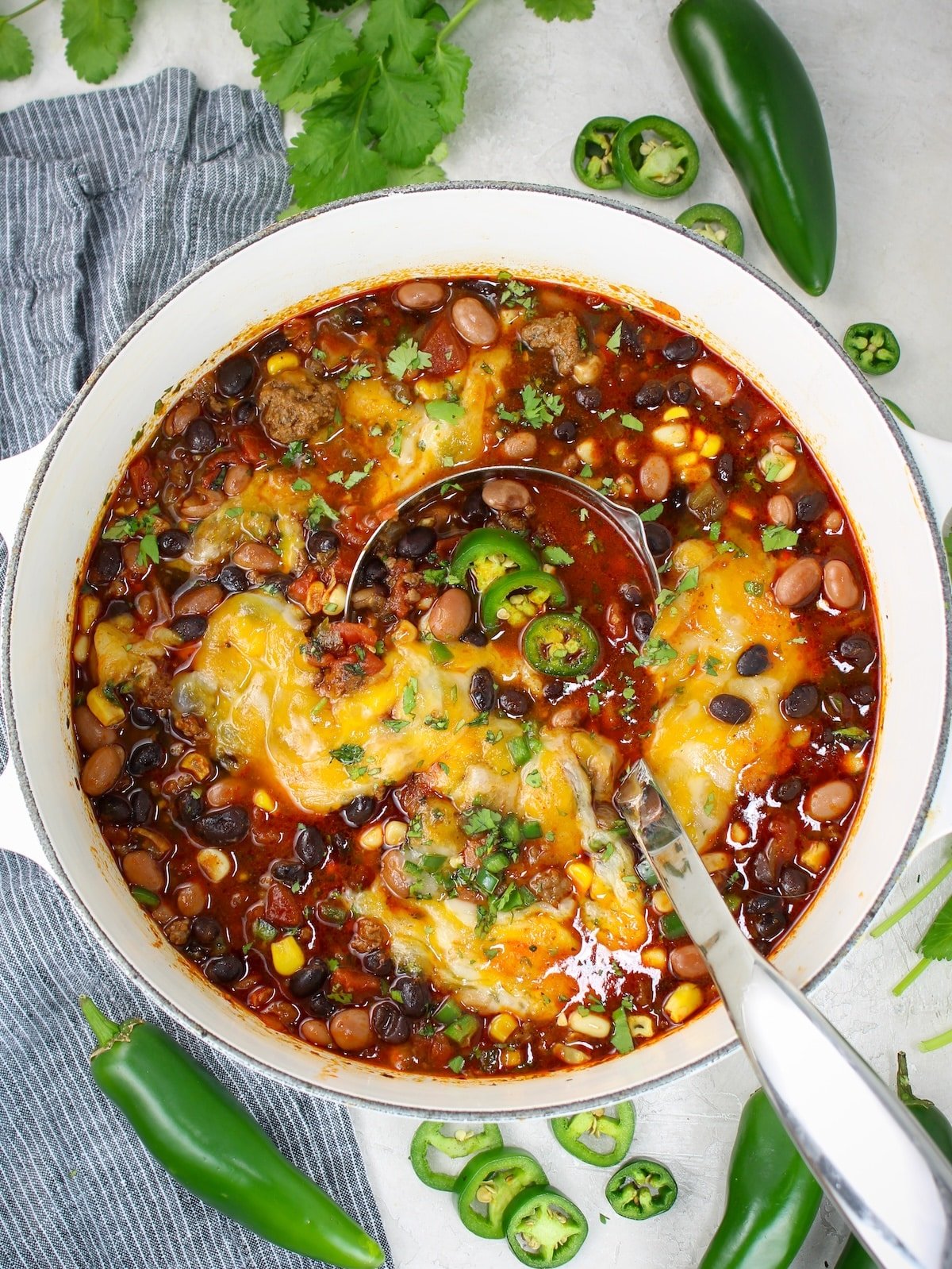 A large pot of a taco soup recipe topped with melted cheese, jalapeños and cilantro.