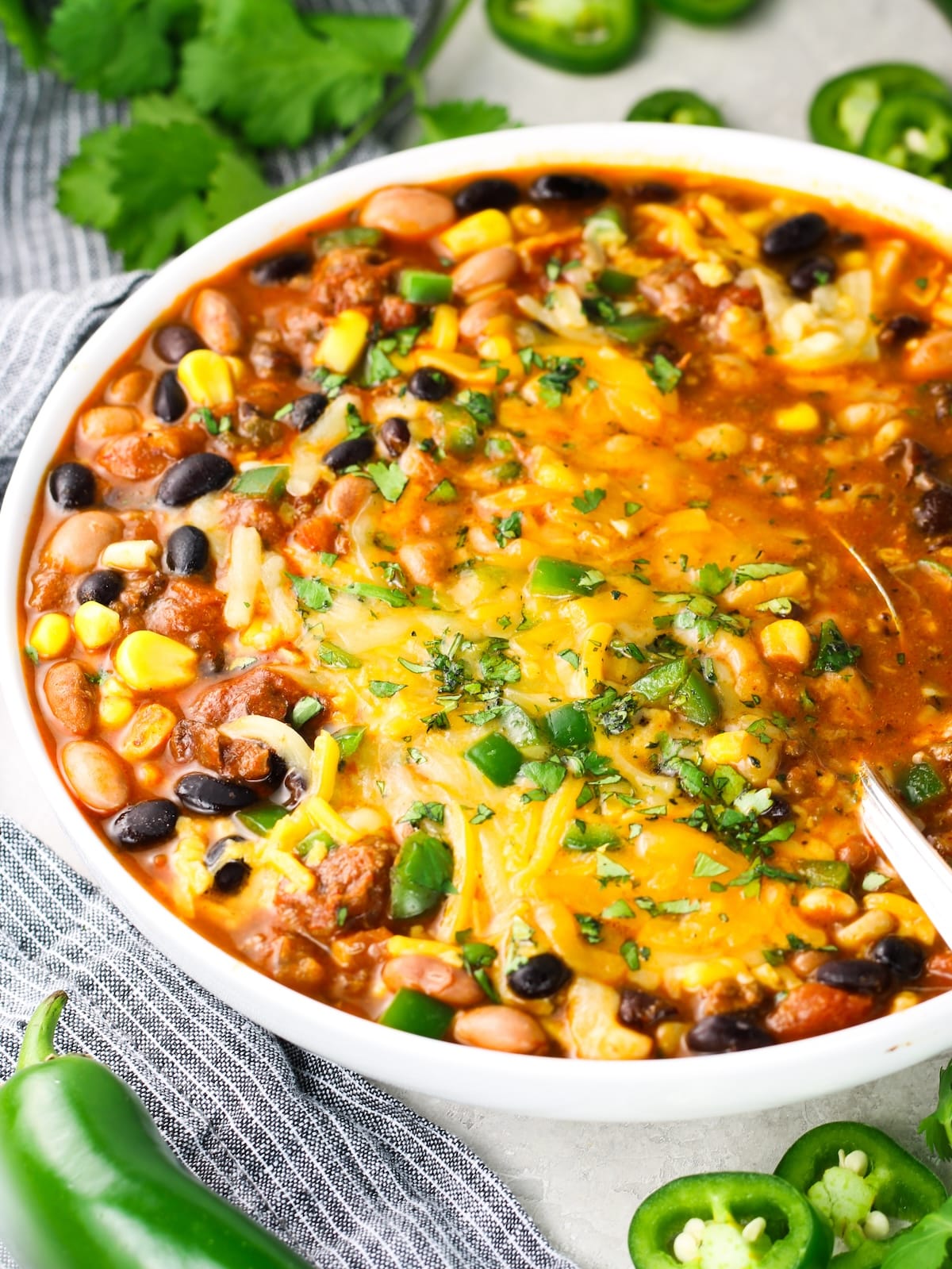 A bowl of Mexican soup with melted cheese, diced jalapeños and cilantro.