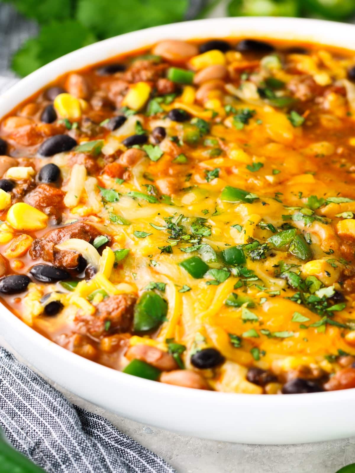 A close-up photo of a bowl of Mexican soup with melted cheese, diced jalapeños and cilantro.