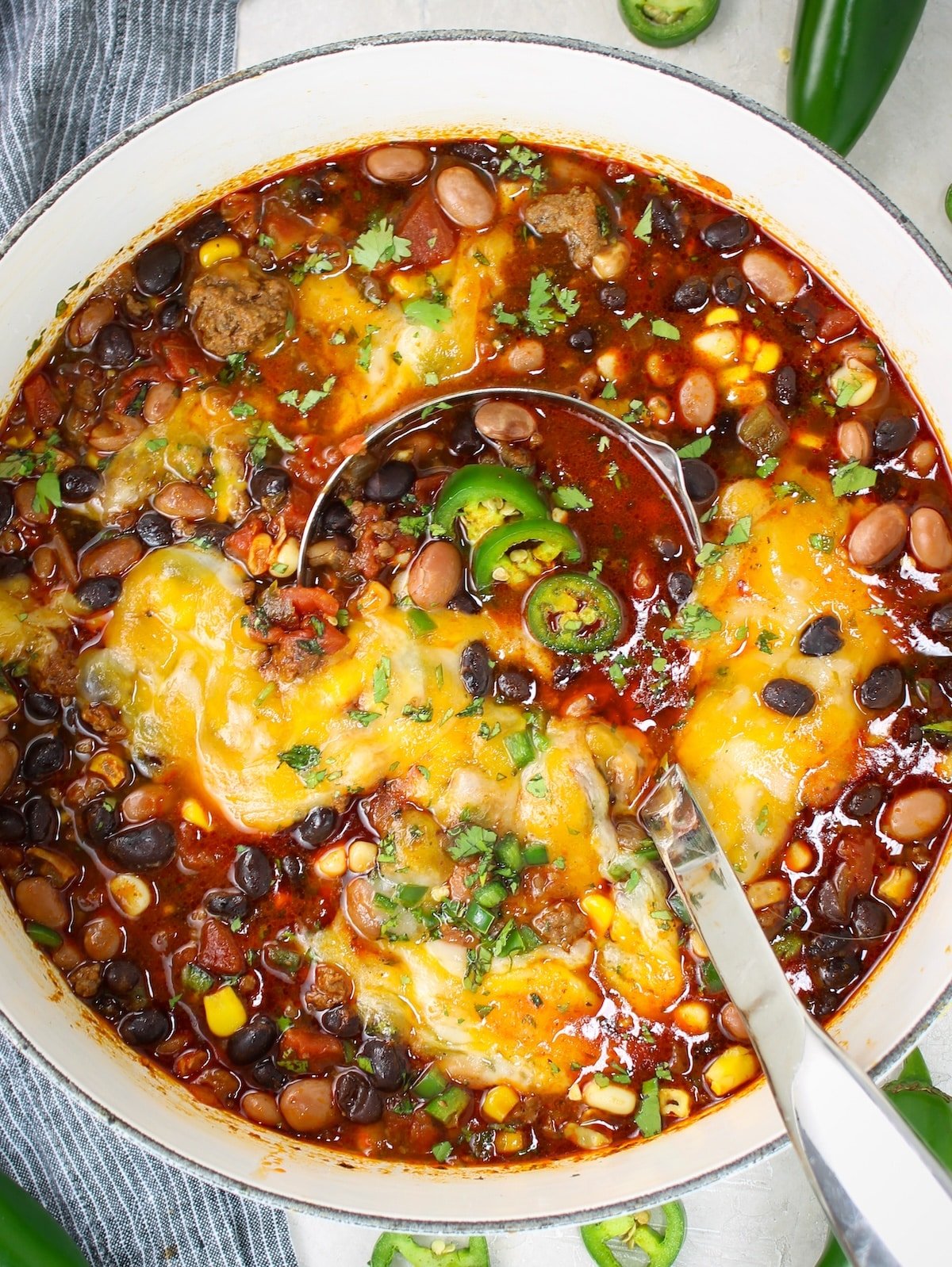 A large pot with taco soup topped with cheese, cilantro and jalapeños.