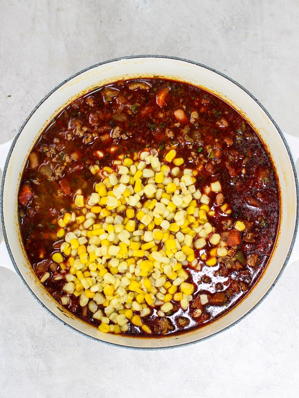 Adding frozen sweet corn to a pot of cooked ground beef, Mexican spices, beef bone broth, veggies, canned tomatoes and tomato sauce.