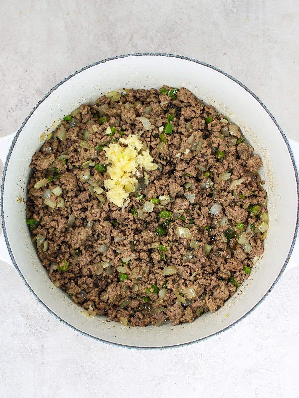 Adding garlic to a pot of cooked ground beef, onions, and jalapeños.