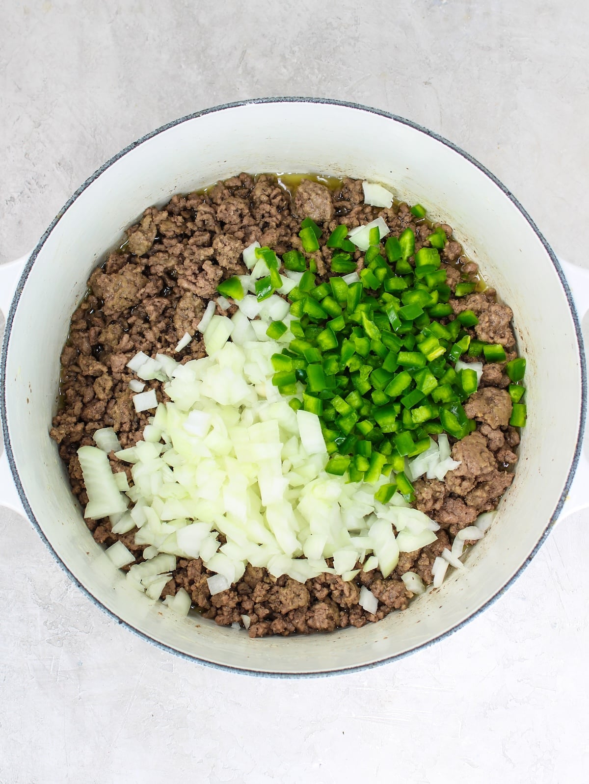 Cooked ground beef in a soup pot with raw onions and jalapeños.