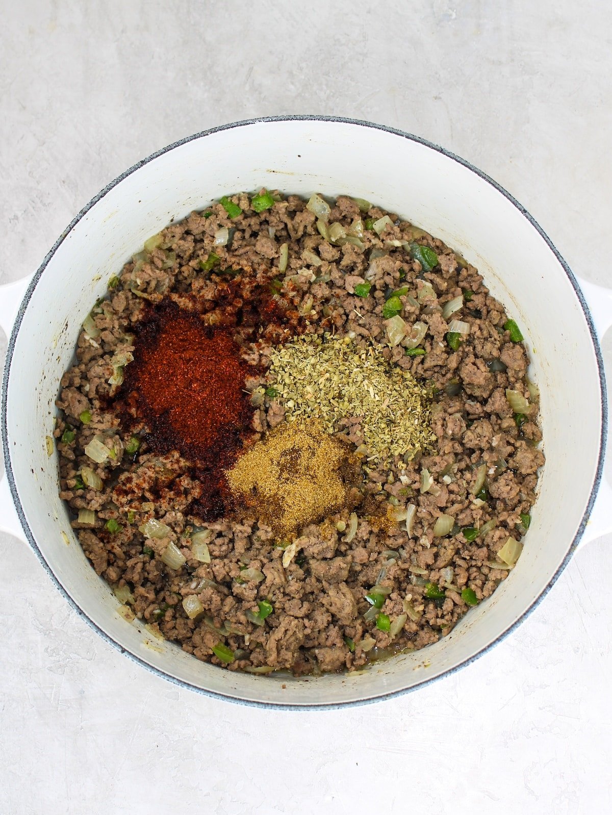 Adding spices to the cooked ground beef, onion, garlic and jalapenos.