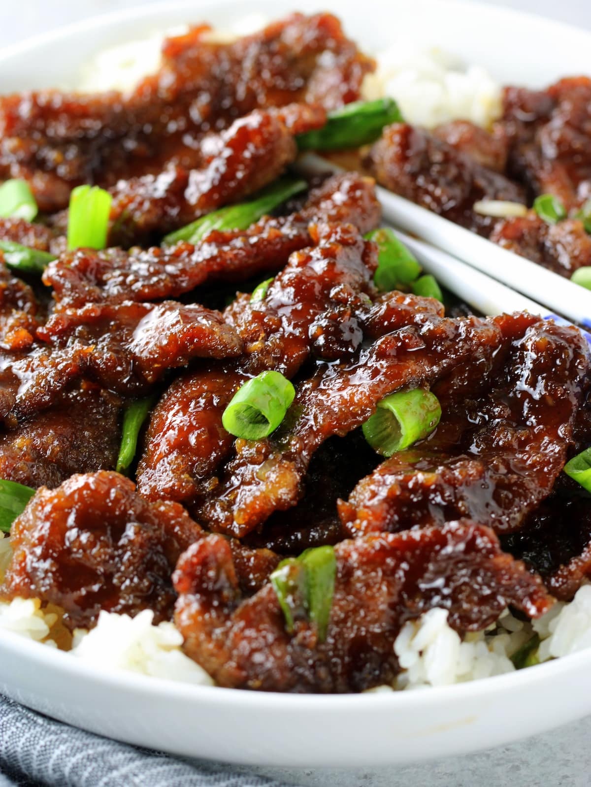 A close up of a plate of food with chopsticks and Mongolian beef.
