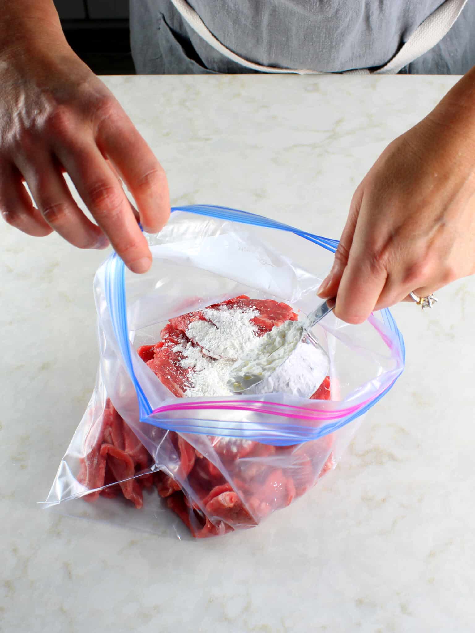 Adding cornstarch to thinly sliced beef.