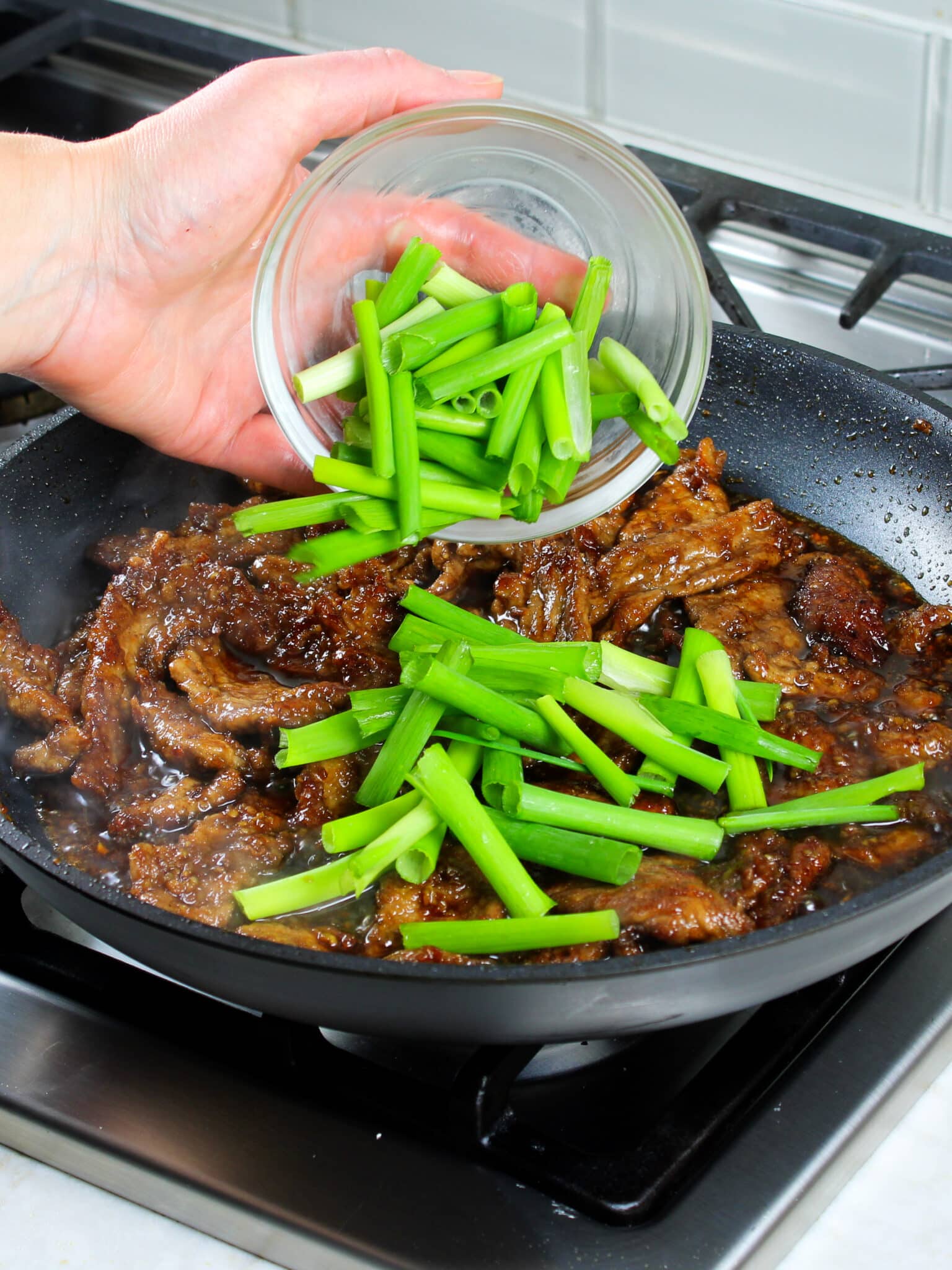 Sprinkling the sliced green onions into the panfried beef and Mongolian sauce.