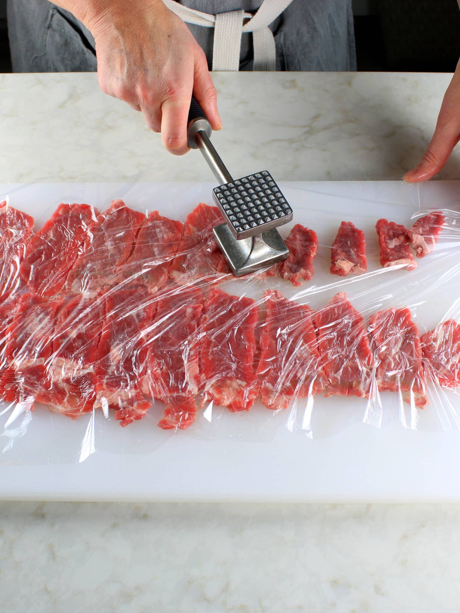 Flattening thinly sliced beef with a meat pounder.