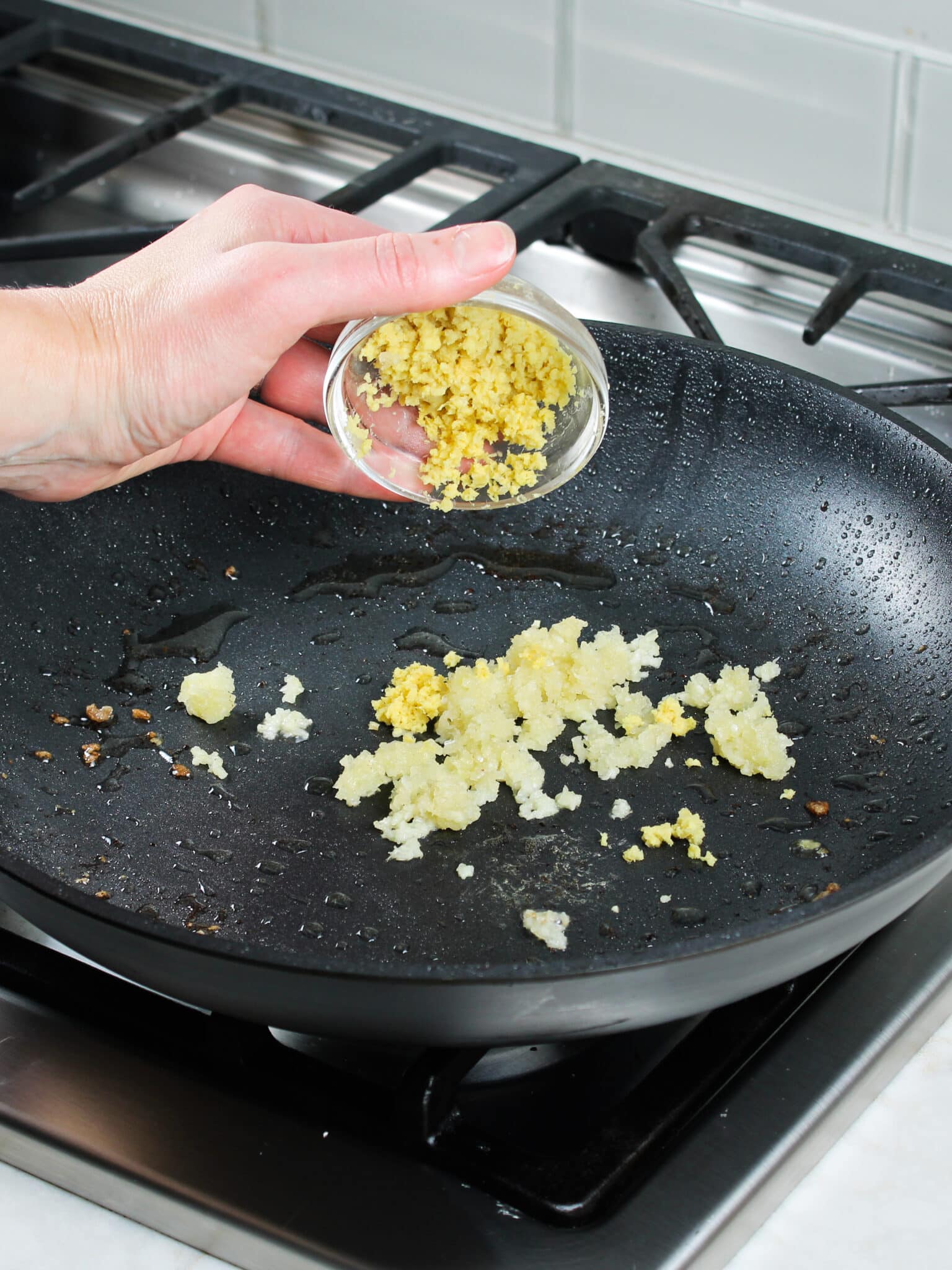 Adding fresh grated ginger into a saute pan with garlic and oil.