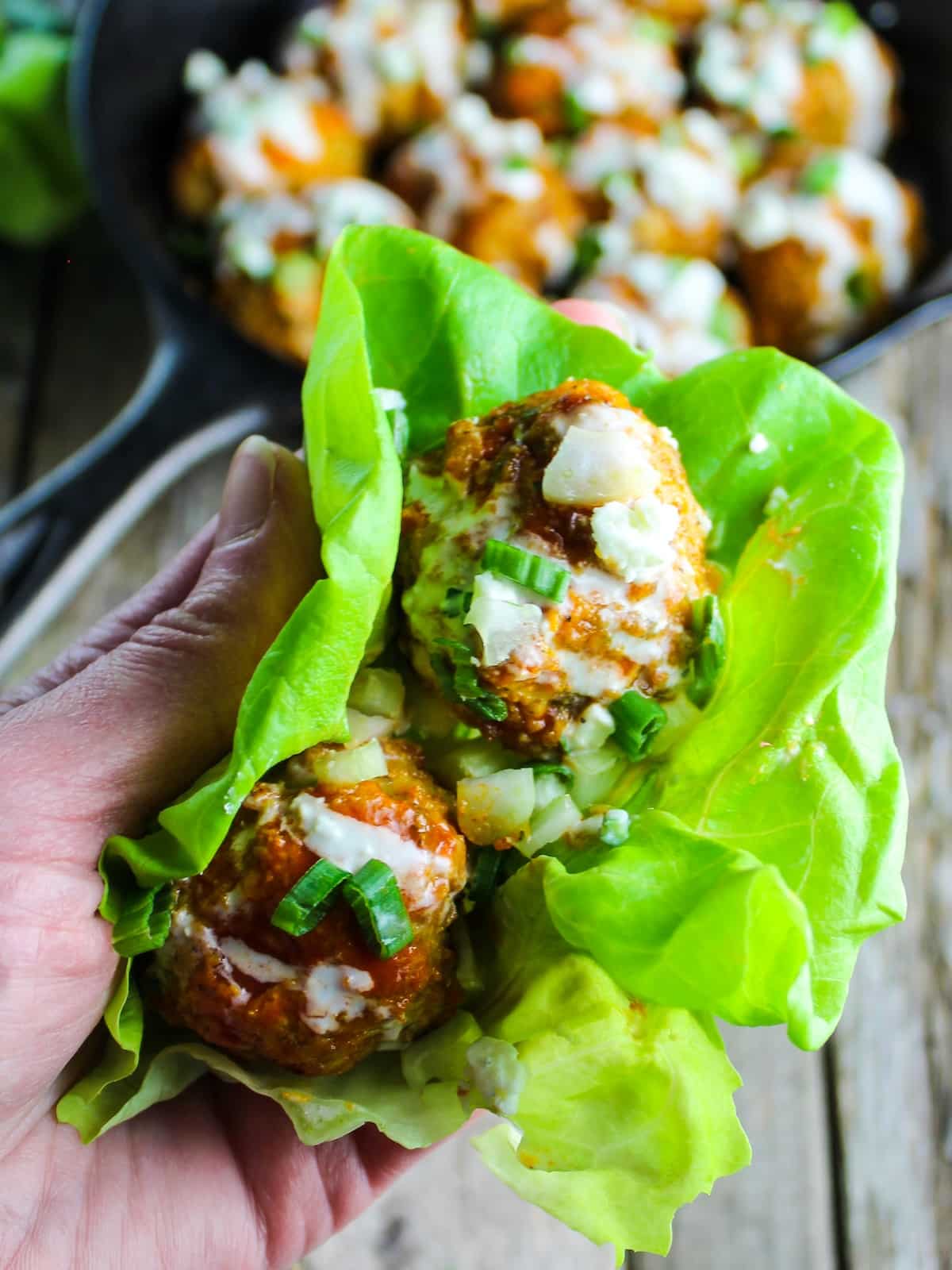 Someone holding two buffalo-flavored meatballs in a lettuce wrap.