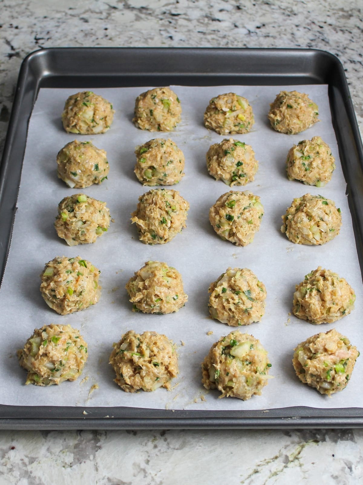 A baking sheet lined with parchment paper with meatballs ready to be baked.
