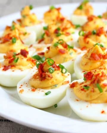 A platter of smoky flavored deviled eggs with bacon and chives.