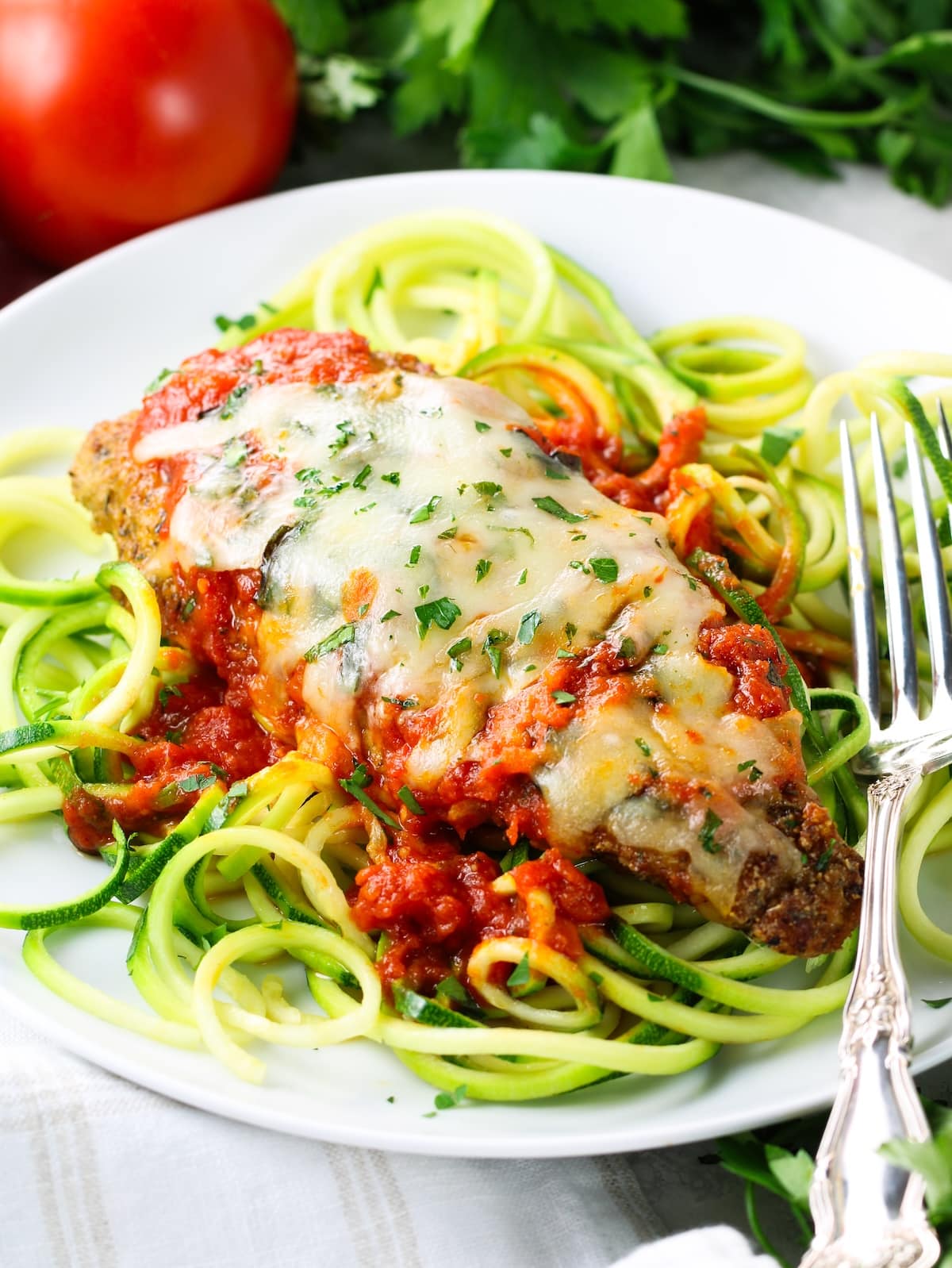 Serving Platter with Baked Chicken Parmesan (Low Carb & Gluten Free) Healthy baked chicken Parmesan on a plate of zoodles with tomato sauce and melted shredded mozzarella cheese.