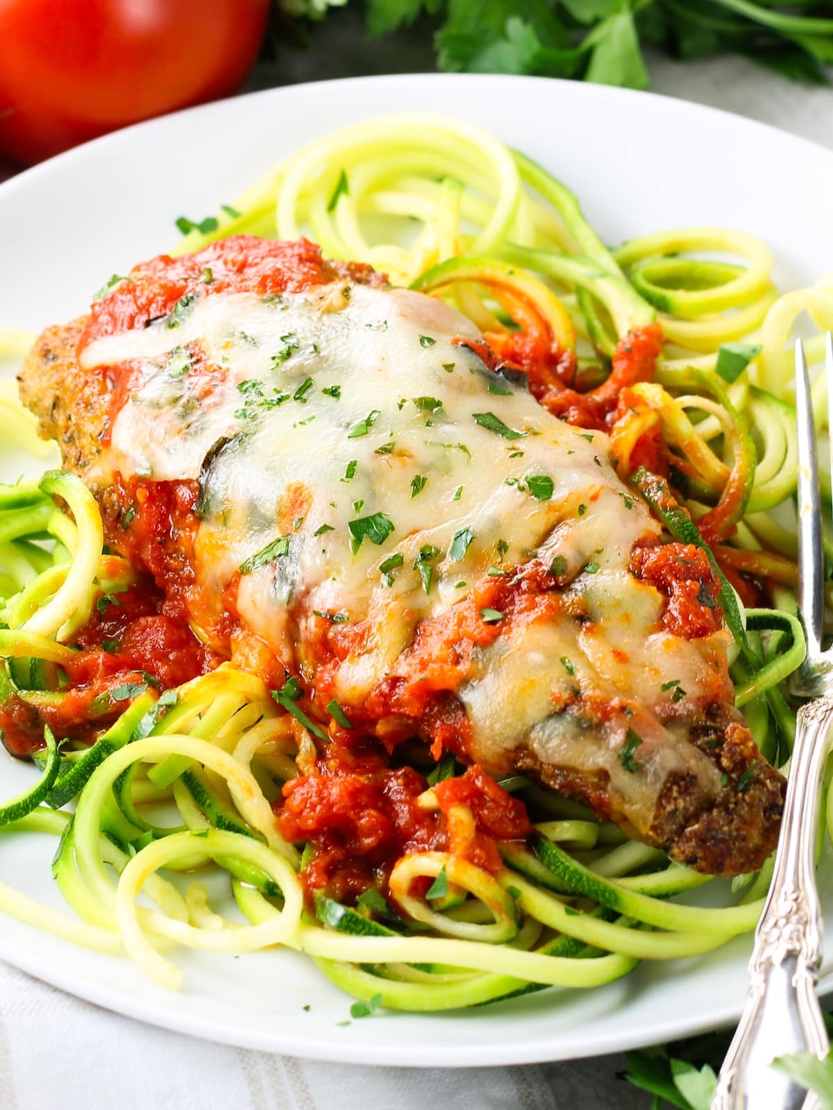 Gluten Free Chicken Parmesan on a serving platter Delicious chicken parm on a plate with zoodles with marinara sauce and melted shredded mozzarella cheese.