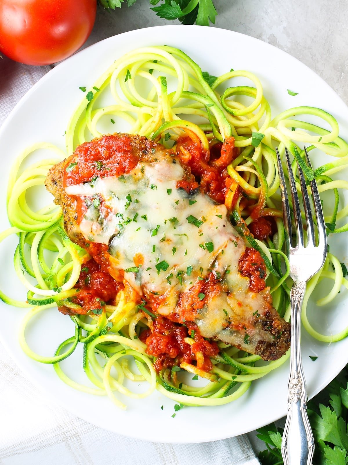 Plate of Baked Chicken Parmesan on zucchini noodles Baked Chicken Parmesan on zucchini noodles with tomato sauce and melted shredded mozzarella cheese.