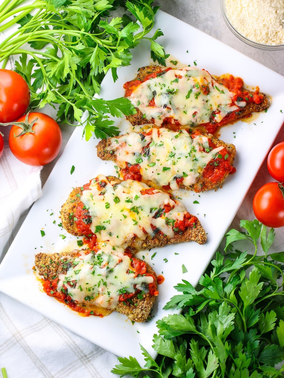 Oven Baked chicken cutlets on a large platter with tomato sauce, melted mozzarella cheese and fresh basil and parsley.