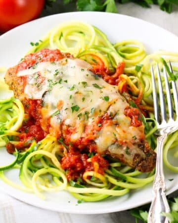 A breaded and baked chicken cutlet on zucchini noodles with tomato sauce and melted shredded mozzarella cheese.