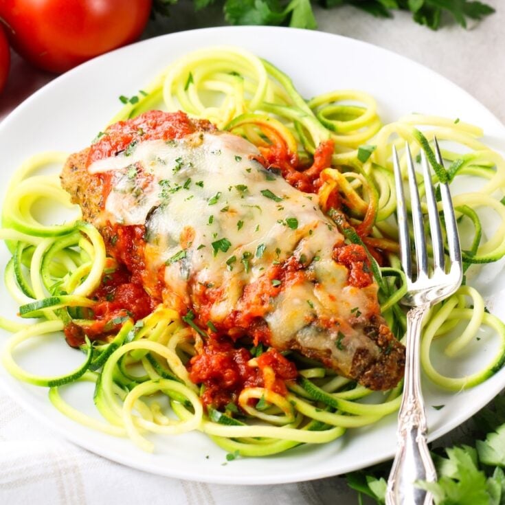 A breaded and baked chicken cutlet on zucchini noodles with tomato sauce and melted shredded mozzarella cheese.