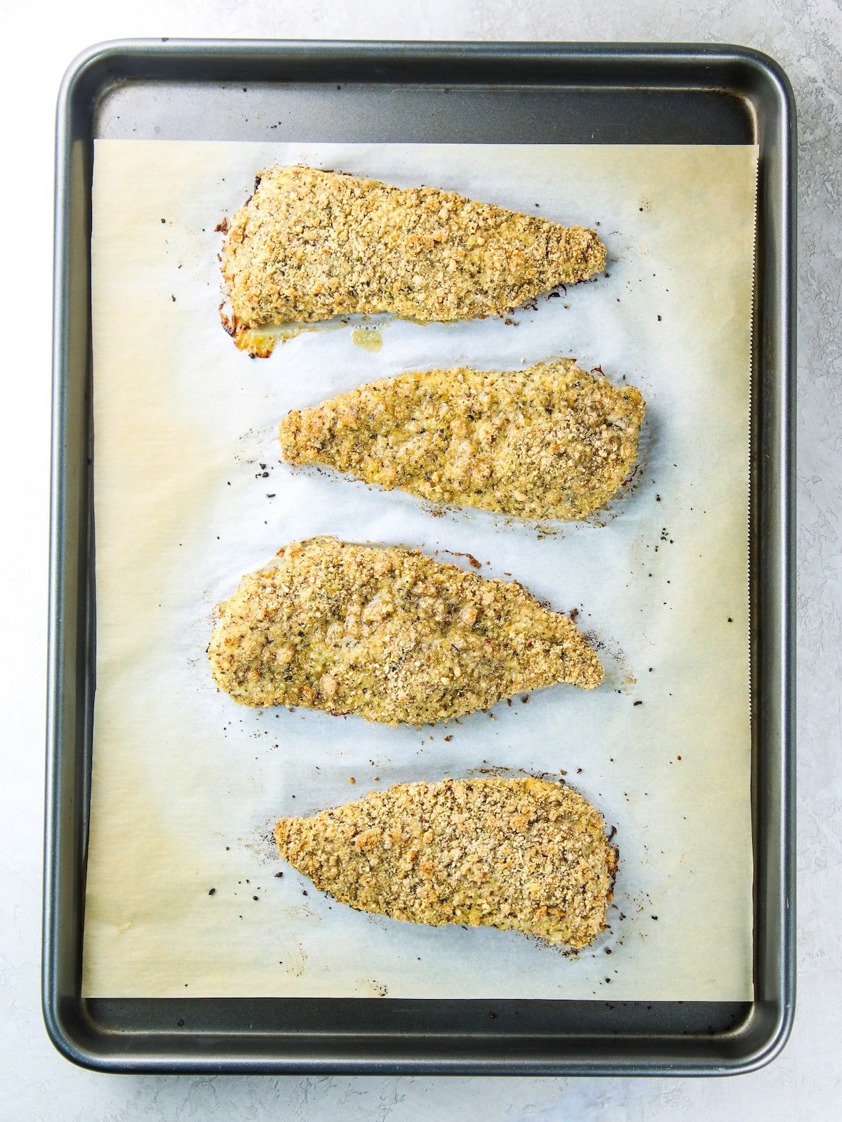 Low Carb Chicken Parmesan on a baking sheet after cooking Baked chicken breasts that have been coated in a bread crumb mixture with Italian seasonings and Parmesan cheese.