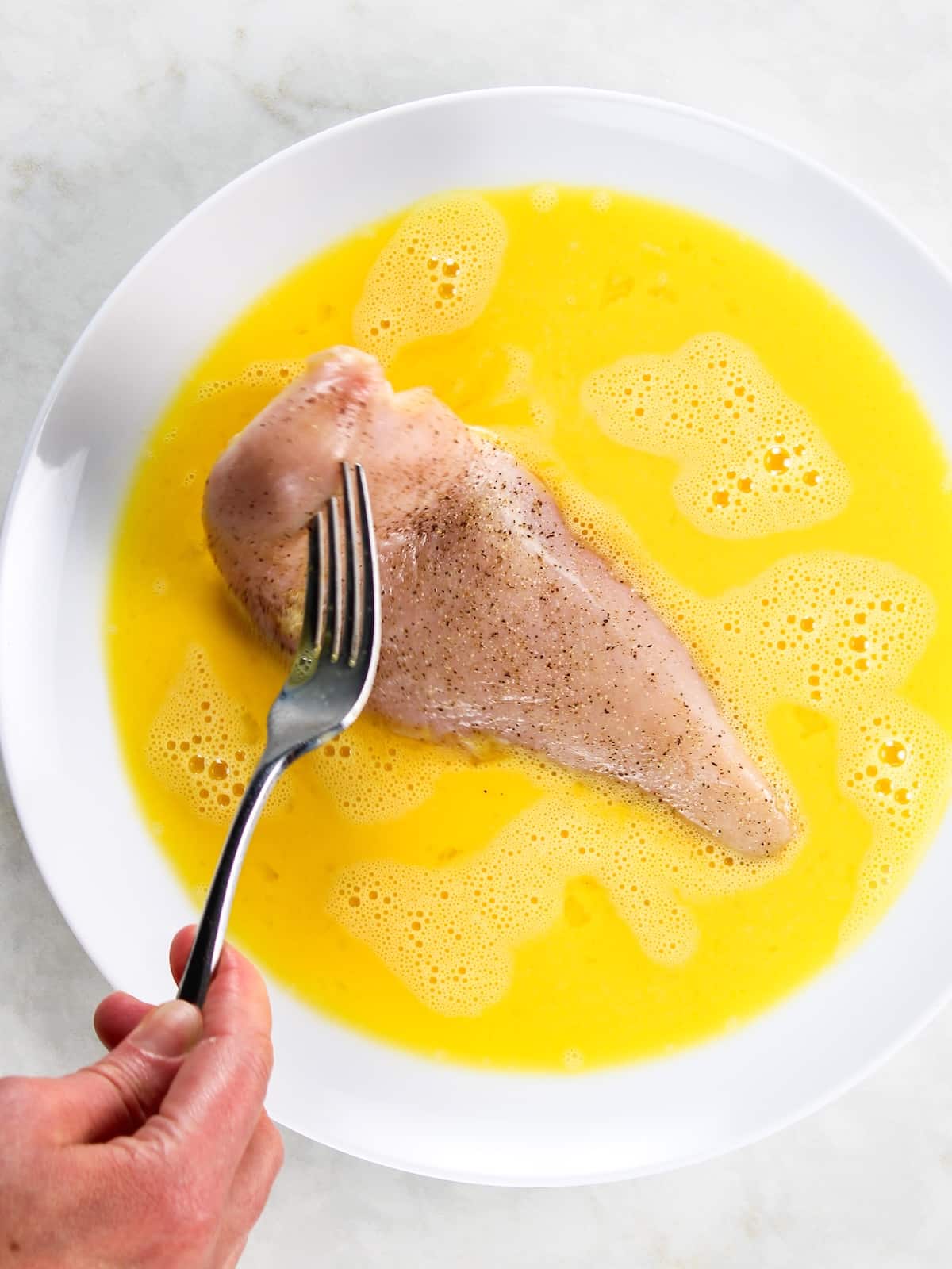 Chicken breast being dipped in a plate with egg wash Chicken parmesan recipe - a chicken cutlet dipped in egg mixture.
